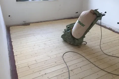 Schleifen eines Dielenbodens der mit Farbe gestrichen wurde Maschine zum Abschleifen eines Holzbodens in einem leerstehenden Raum.