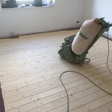 Abgeschliffene Dielen Holzboden mit einer Schleifmaschine in einem lichtdurchfluteten Raum.