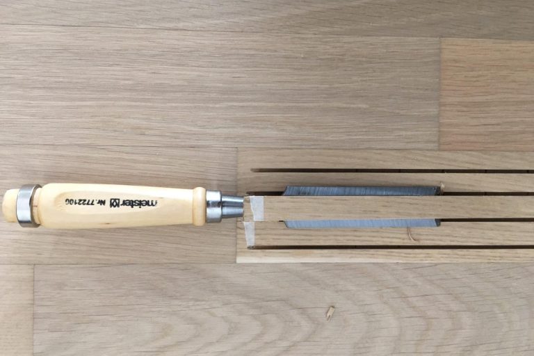 Austausch eines Schadhaften Parkettstabes Holzwerkzeug mit Holzgriff und schlanker Klinge auf einer Holzoberfläche.