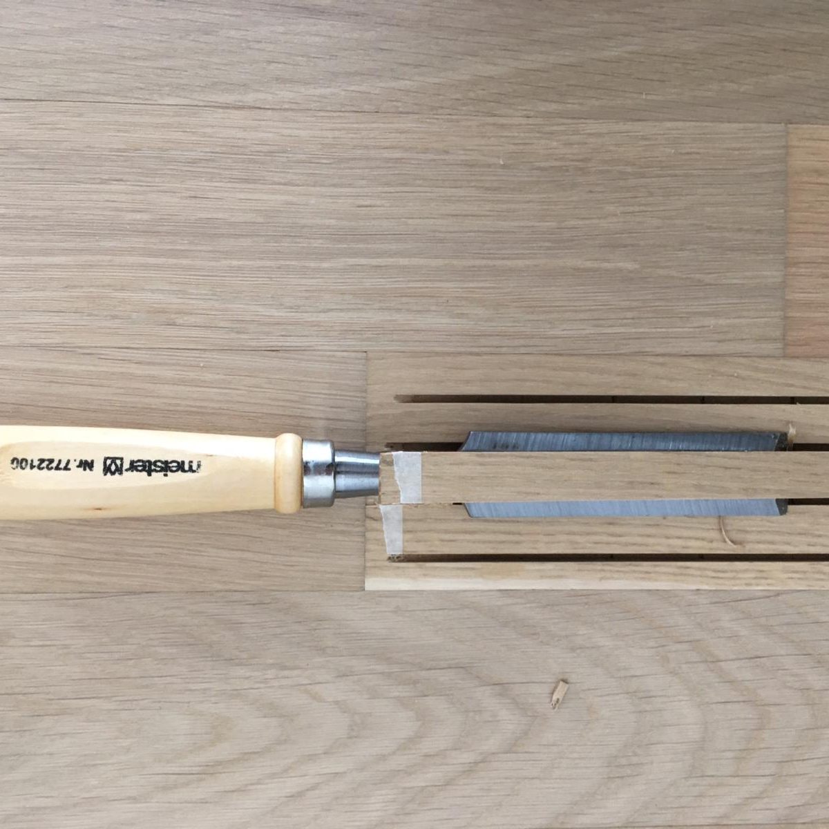 Austausch eines Parkettstabes Holzbeitel mit Holzgriff liegt auf einer Holzoberfläche neben einem Holzstück.