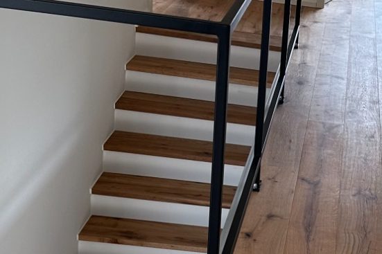 Treppenstufen mit Eiche Landhausdielen verlegt Holztreppe mit weißen Stufen und einem minimalistischen schwarzen Geländer.