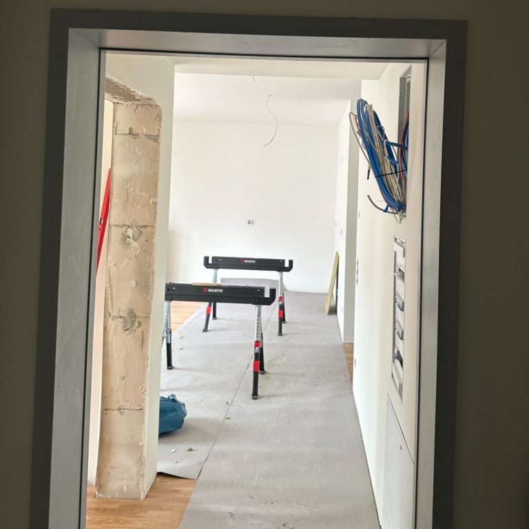 Stahlzargen Einbau Blick durch eine Tür auf einen leeren Raum mit Baugeräten und Bodenbelag.